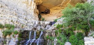 Afqa Grotto in Lebanon showing a water stream running over limestone rocks between green bushes.